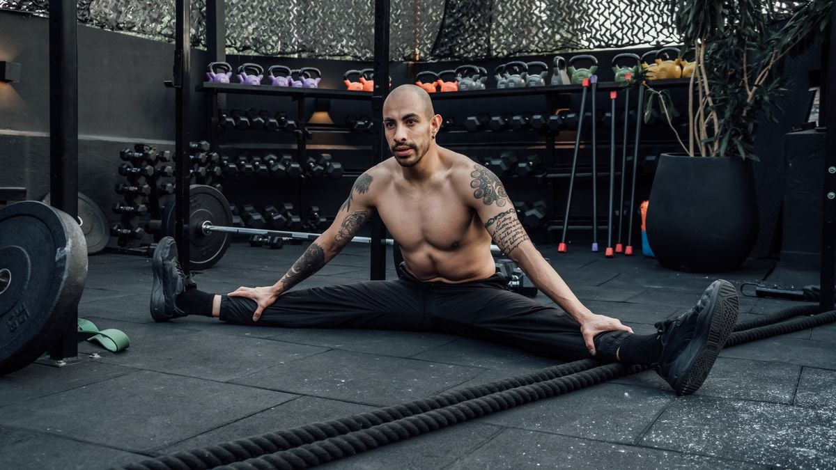 Tattooed man performing a split stretch in a gym, showcasing flexibility and fitness lifestyle in Mexico City.